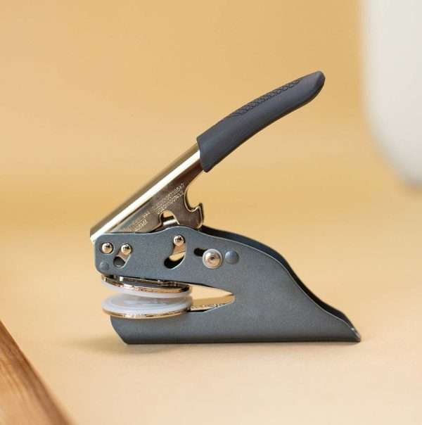 UK handheld embosser with metal handle and circular embossing plate.