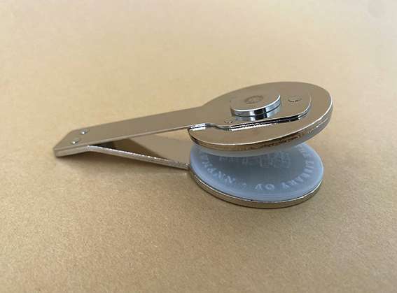 Silver round handheld embosser insert tool on beige background.