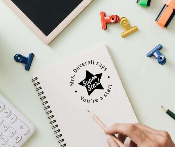 Teacher using custom classroom rubber stamp with star design on student paper.