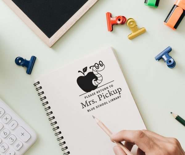 Teacher applying a bookworm -themed stamp on classroom worksheets.