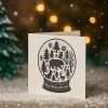 Snow globe Christmas rubber stamp displayed on festive background with lights.